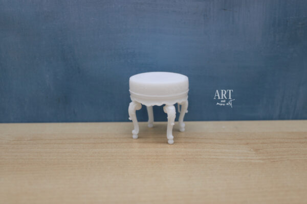 1:12 schaal miniatuur ronde hocker met sierlijke poten, onbewerkt wit en geschikt voor schilderen, geplaatst op een houten oppervlak met een blauwe achtergrond.